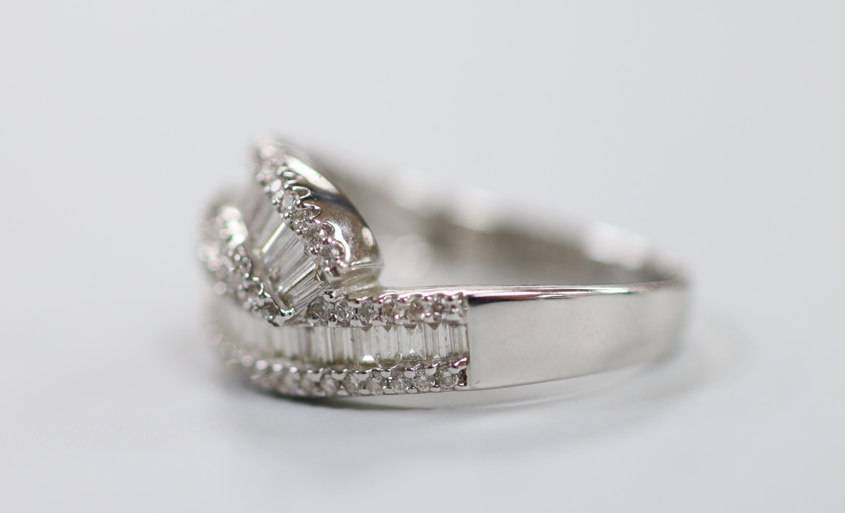 A modern 18ct white gold, baguette cut and diamond chip cluster set crossover ring, size O, gross weight 4.7 grams.